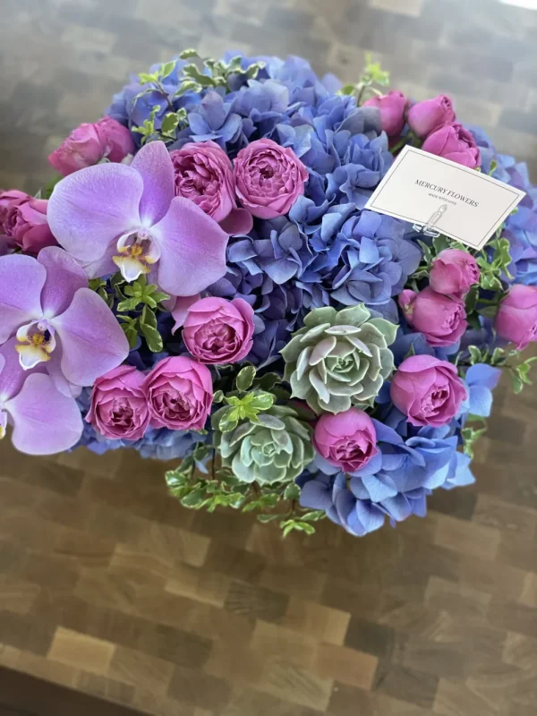 Flower arrangement with orchid and succulents in a glass square vase